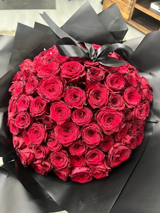 a bouquet of 100 red roses topped with a black bow